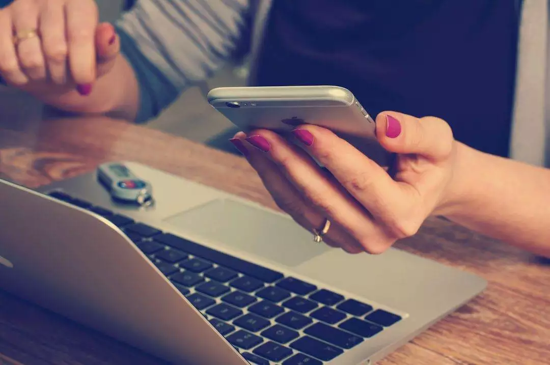 Ultimate Guide to Website Security for Small Businesses Person holding a smartphone while sitting at a desk with an open laptop and USB flash drive—perfect setup for a WordPress web designer working on affordable web design services.