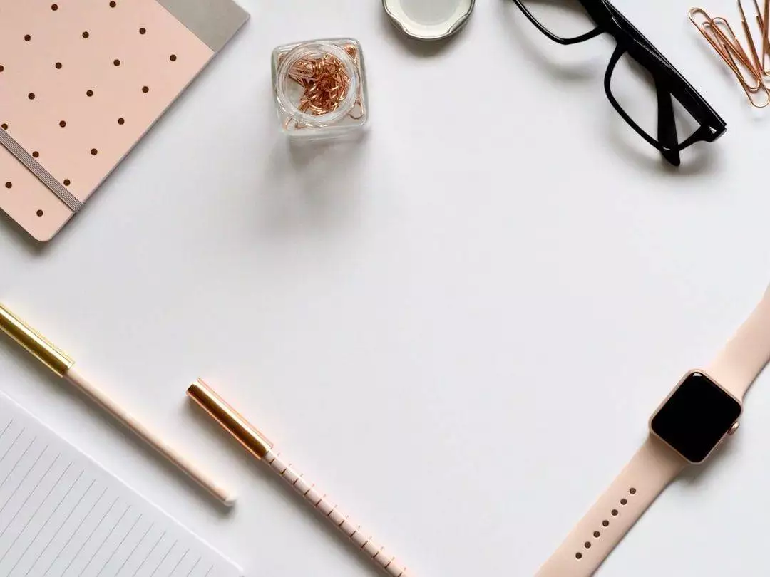 Mastering Small Business Website Solutions: A Comprehensive Guide A flat lay of a notebook, pen, pencil, paper clips, glasses, smartwatch, and a jar of rose gold binder clips on a white desk—perfect inspiration for any WordPress web designer or small business website design project.