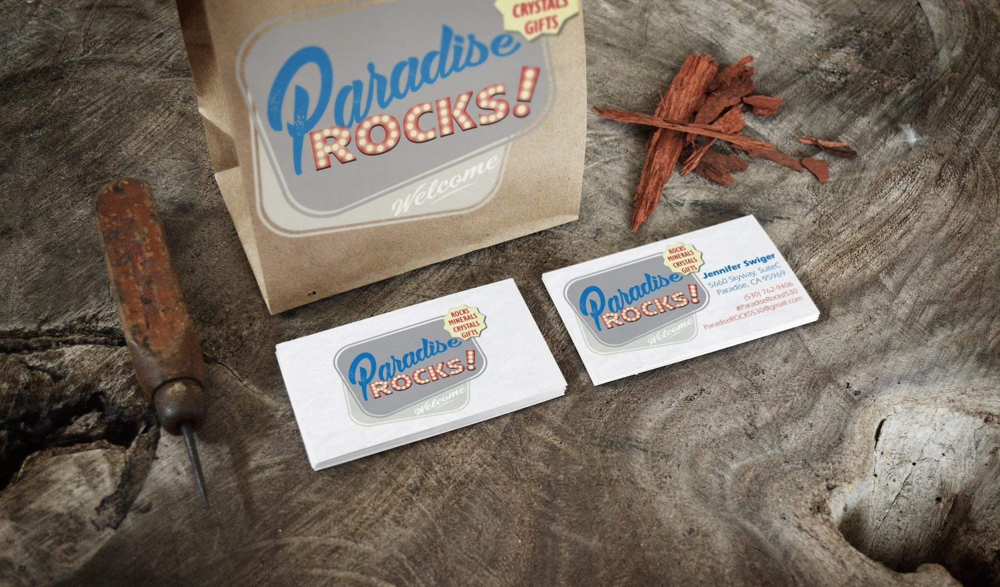 Portfolio Two “Paradise Rocks!” business cards, a paper bag, a rusty tool, and wood pieces are displayed on a textured wooden surface—perfect inspiration for small business website design.All-inclusive Website Design Services