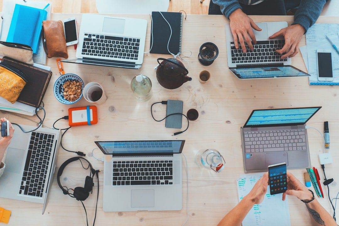 Effortless Website Maintenance Guide for Non-Profits A group of people work at a cluttered table with laptops, notebooks, snacks, and headphones—collaborating like a professional website design company or WordPress web designer focused on website maintenance and support.