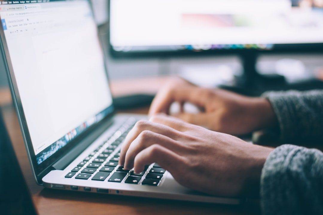 A person types on a laptop keyboard at a desk, with a blurred computer monitor in the background, representing the work of a professional website design company.