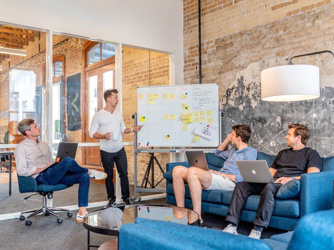 Four people with laptops sit and listen as one person stands and presents information on a whiteboard in a modern office—typical of a professional website design company focused on collaboration and creativity.