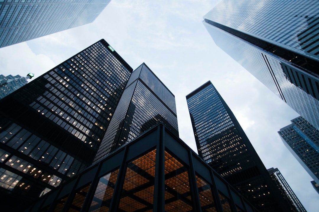 Tall glass and steel office buildings rise against a cloudy sky, viewed from street level in a modern city business district—reflecting the ambition of a professional website design company.