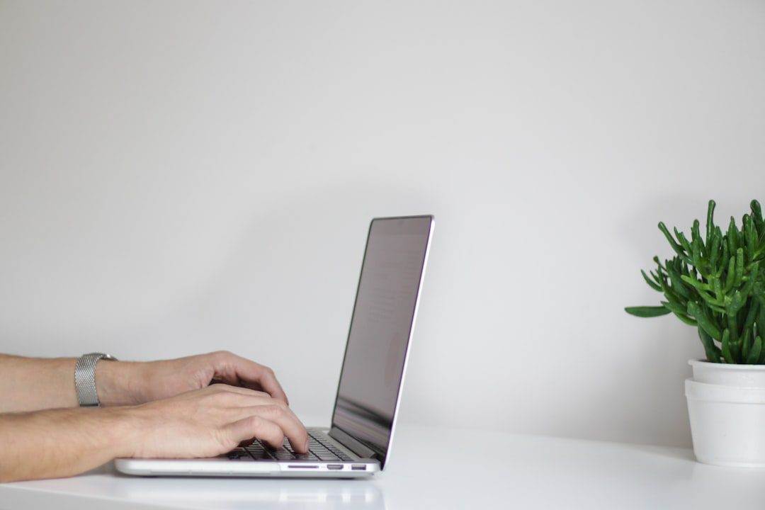 Ultimate Guide to Efficient Website Maintenance Services Hands typing on a laptop placed on a white desk, with a small potted plant beside the computer—a workspace perfect for a web designer near me focused on creativity and detail, set against a plain white background.