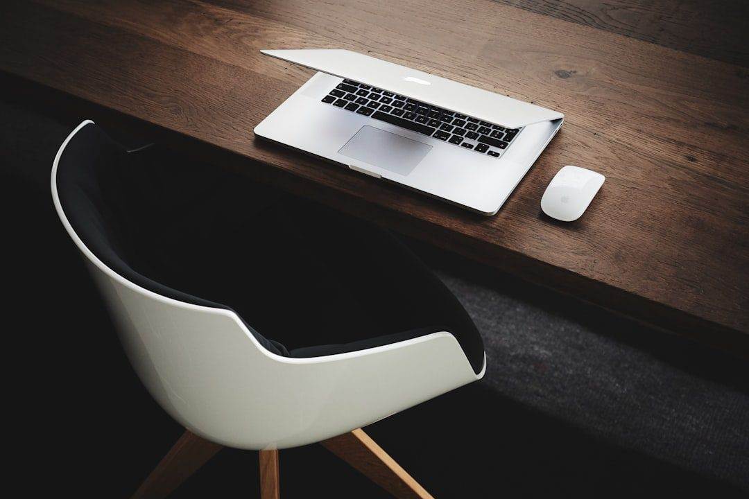 A partially closed laptop, white wireless mouse, and modern white chair on a dark wooden desk—perfect inspiration for small business website design.