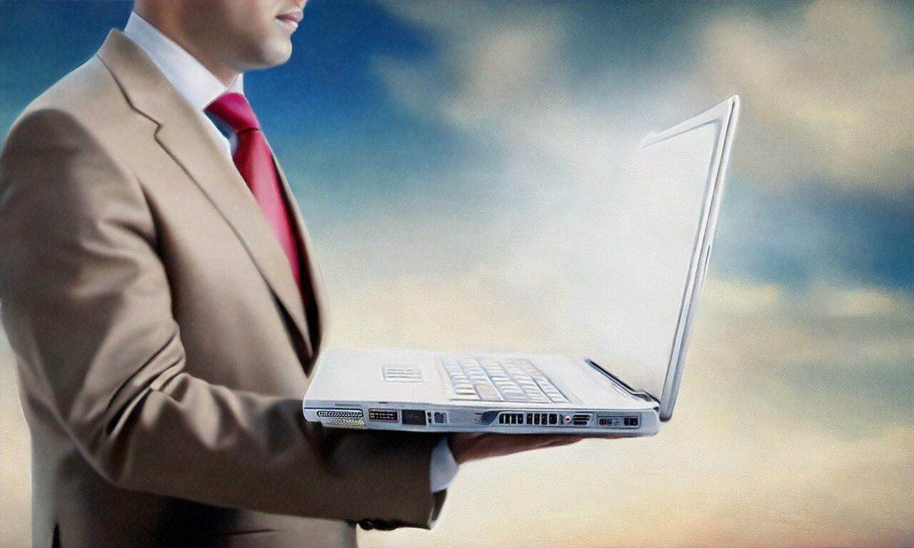 A man in a beige suit and red tie holds an open laptop against a blurred sky background, ready to discuss small business website design.