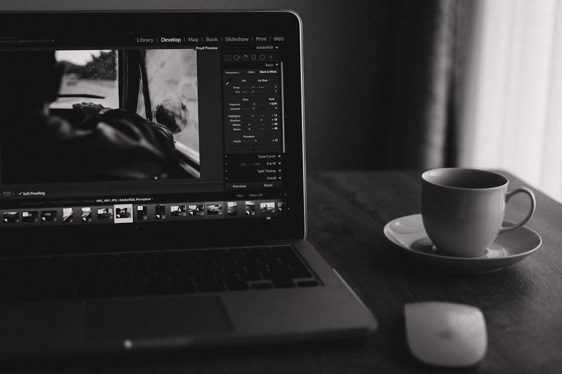 Choosing a Web Design Partner: Tips for Businesses Seeking Growth A laptop displaying photo editing software sits on a desk next to a computer mouse and a cup of coffee on a saucer, perfect for any WordPress web designer focused on affordable web design services.
