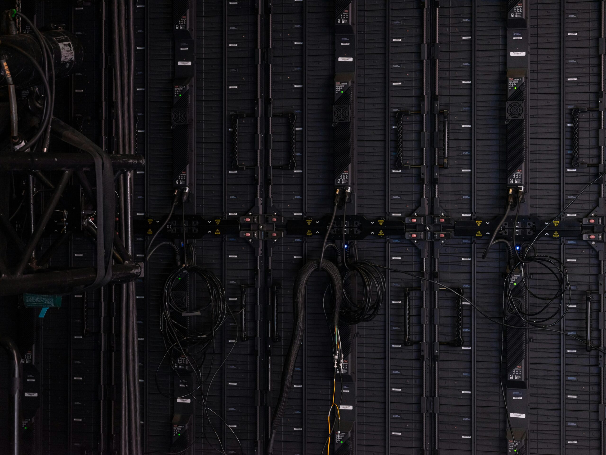 A wall of black electronic equipment with multiple cables plugged in and coiled, showing the technical backside of an LED panel or server setup.