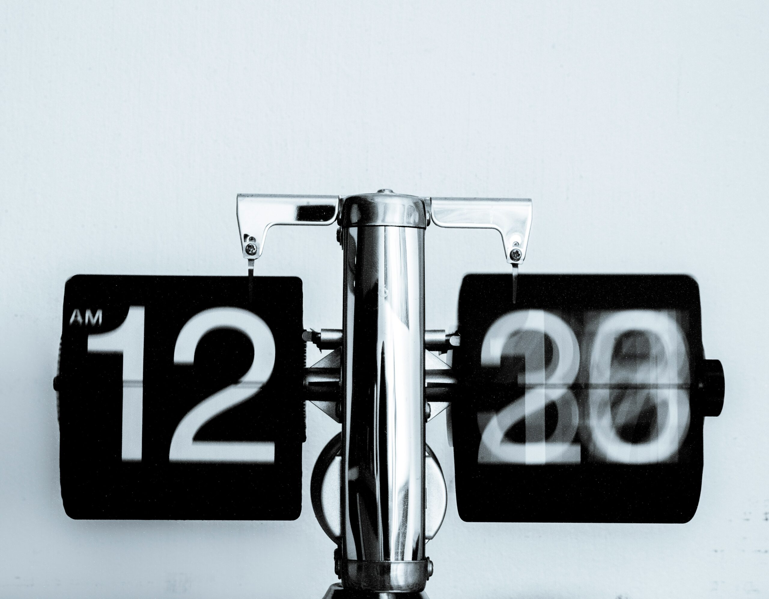 Close-up of a retro flip clock showing the numbers flipping from 12:20 AM, with motion blur on the right side indicating movement.