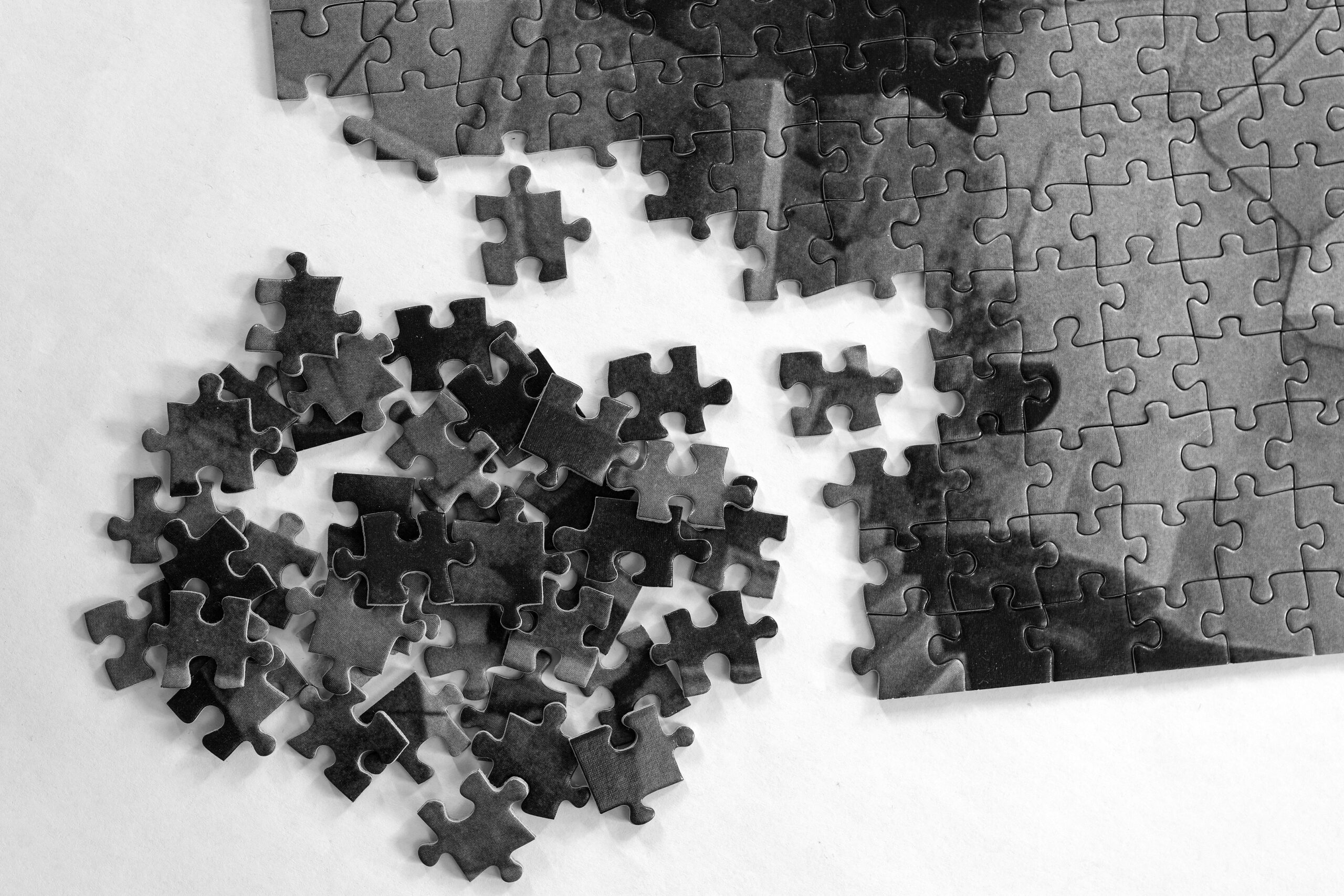 A partially completed jigsaw puzzle with scattered loose pieces on a white surface, shown in black and white.