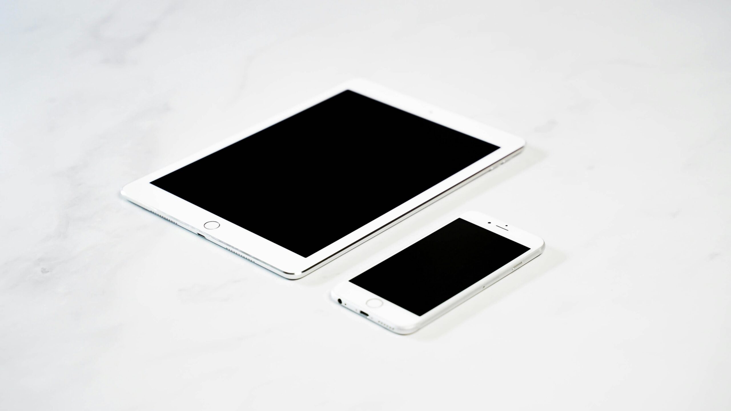 Stop Wasting Time Updating Plugins: Why Local Non-Profits Are Switching to WaaS A white tablet and a white smartphone are placed side by side on a light, marble-like surface. Both devices have black screens.
