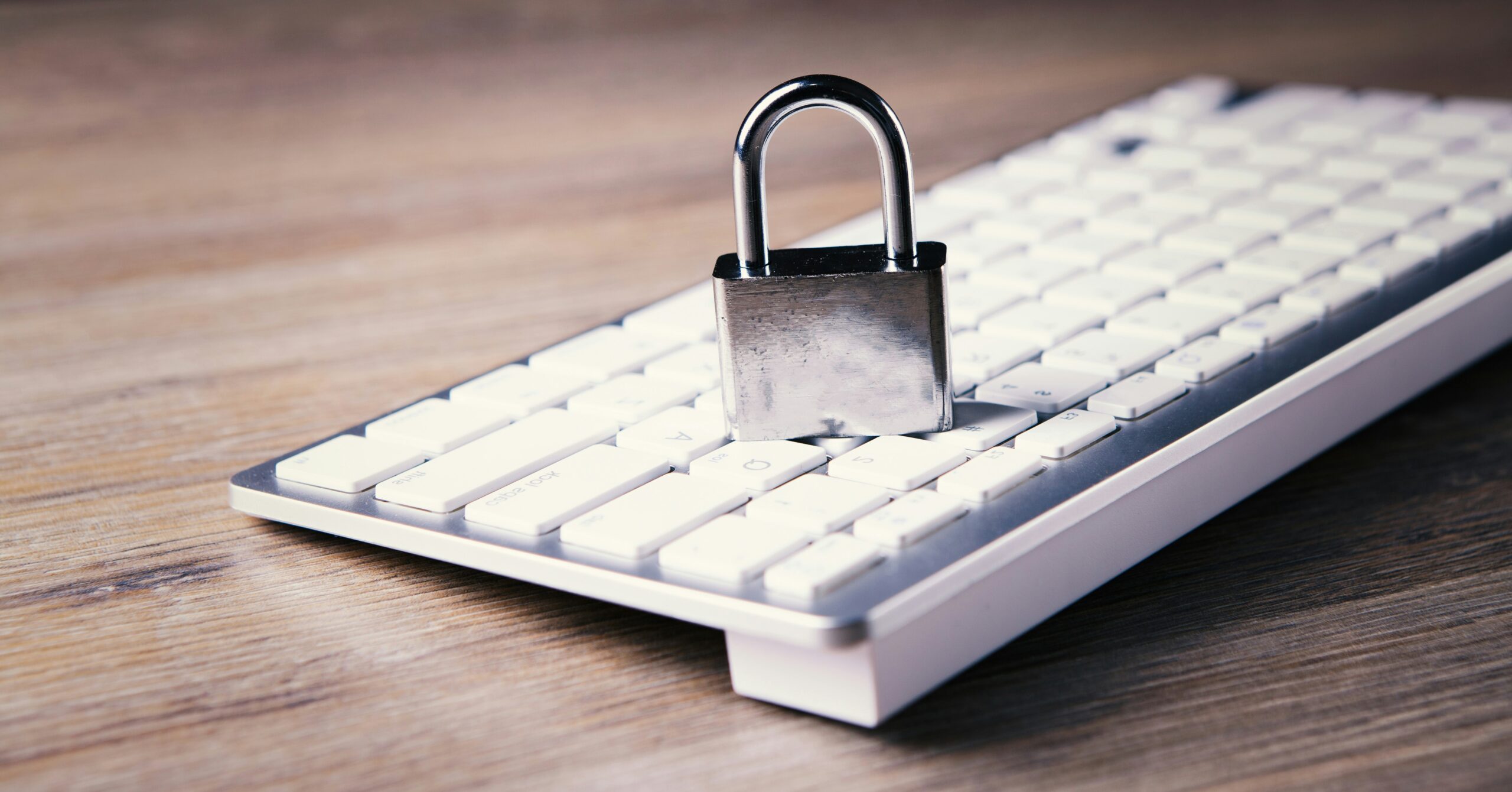 A metal padlock placed on a white computer keyboard on a wooden desk, symbolizing cybersecurity or data protection.